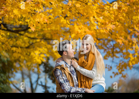 Portrait of happy woman sitting on man's lap in park during autumn Stock Photo