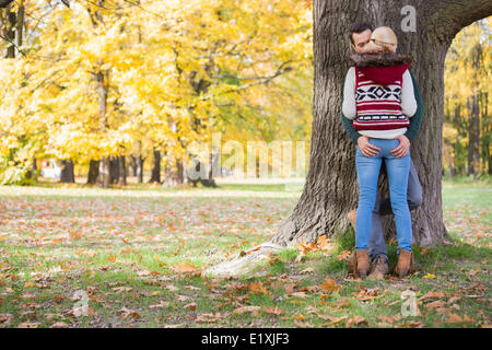 Passionate couple against tree trunk in park during autumn Stock Photo