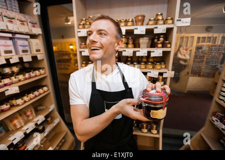 Cheerful salesman holding jar of jam in grocery store Stock Photo