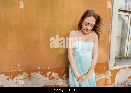 Shy teenage girl in tube dress standing against wall Stock Photo