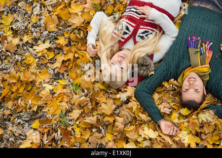 High angle portrait of young couple lying on autumn leaves at park Stock Photo