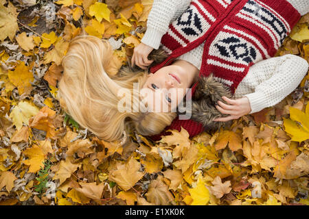 High angle view of thoughtful young woman lying on autumn leaves in park Stock Photo