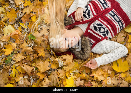 High angle portrait of young woman lying on autumn leaves in park Stock Photo