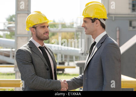 Young businessmen in hard hats shaking hands at construction site Stock Photo