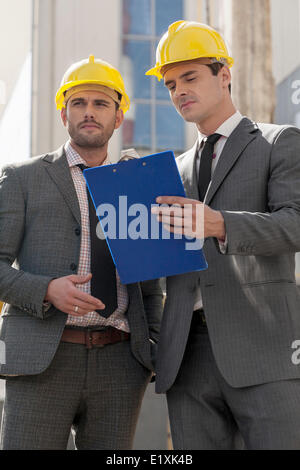 Young male engineers with clipboard discussing at construction site Stock Photo