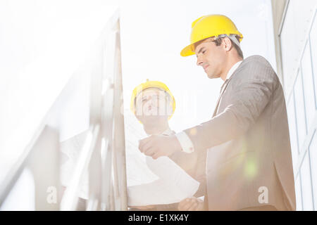 Low angle view of young businessman in hard hats reviewing blueprint on stairway Stock Photo