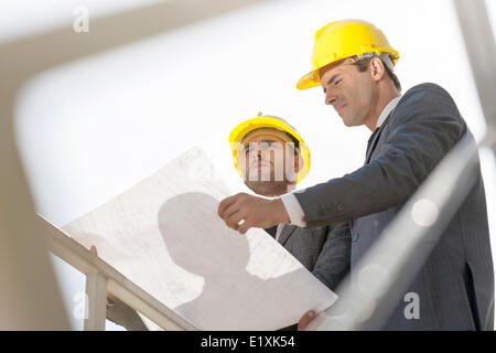 Low angle view of young businessmen holding blueprint against clear sky Stock Photo