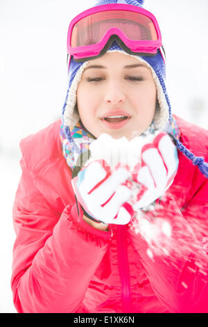 Young woman wearing winter coat blowing snow outdoors Stock Photo
