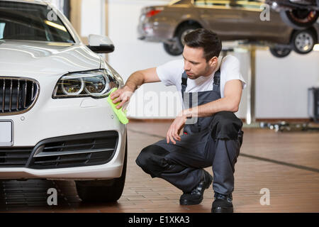 Full length of maintenance engineer cleaning car in workshop Stock Photo