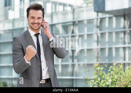 Portrait of successful young businessman using cell phone against office building Stock Photo