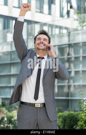 Excited young businessman using cell phone outside office Stock Photo