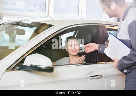 Smiling female customer receiving car key from mechanic in workshop Stock Photo