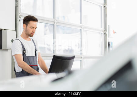 Young male automobile mechanic using computer in repair shop Stock Photo