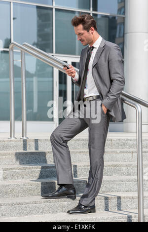 Full length of businessman text messaging through cell phone while standing on steps outside office Stock Photo