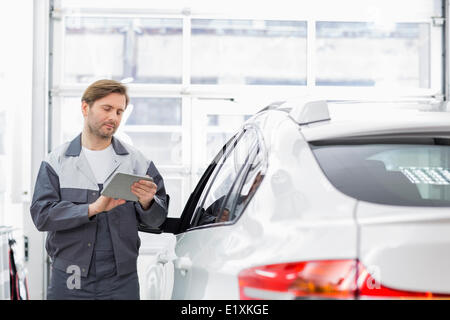 Male repair worker using tablet PC while standing by car in workshop Stock Photo