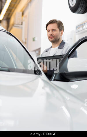 Maintenance engineer holding tablet PC while examining car in repair shop Stock Photo