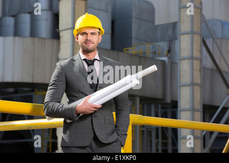Portrait of confident young architect holding blueprints outside industry Stock Photo