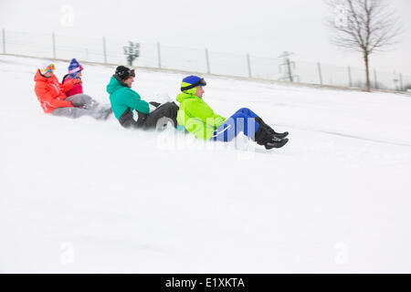 Side view of young friends sledging on snow covered slope Stock Photo