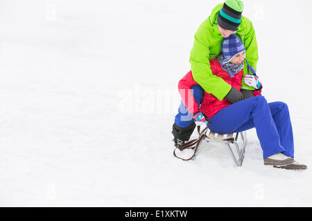 Young man embracing woman on sled in snow Stock Photo