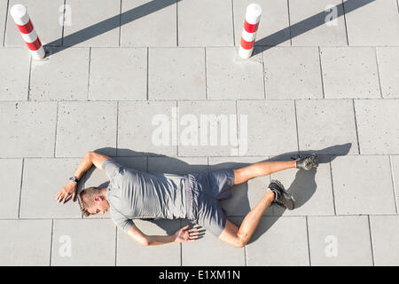 High angle view of tired sporty man lying on sidewalk Stock Photo