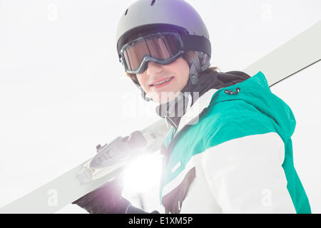 Portrait of smiling young man carrying skis against clear sky