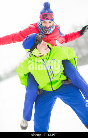 Happy young man giving piggyback ride to woman in snow Stock Photo