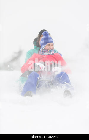 Cheerful young couple sledding in snow Stock Photo