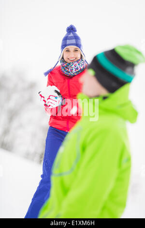Smiling young woman having snowball fight with male friend Stock Photo