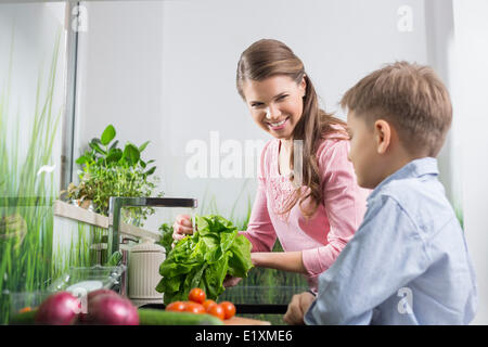 Happy mother and son washing vegetables in kitchen Stock Photo
