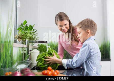 Happy mother looking at son washing vegetables in kitchen Stock Photo