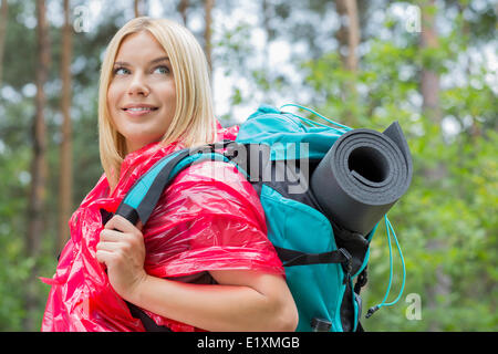 Side view smiling female backpacker in raincoat looking away at forest Stock Photo