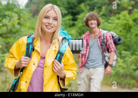 Smiling female backpacker looking away with man standing in background at forest Stock Photo