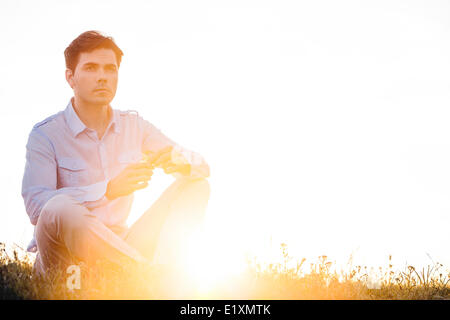 Thoughtful man looking away while sitting on grass against clear sky Stock Photo
