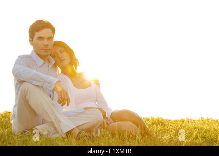 Portrait of confident young man sitting with girlfriend on grass against clear sky Stock Photo
