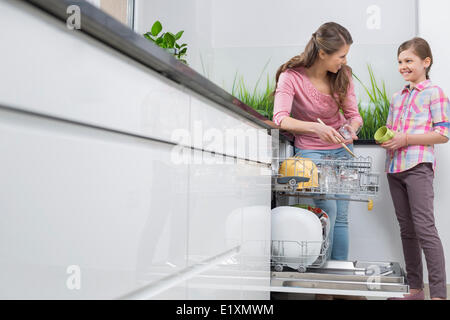 Happy mother and daughter placing glasses in dishwasher at kitchen