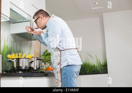 Side view of man tasting food while cooking in kitchen Stock Photo