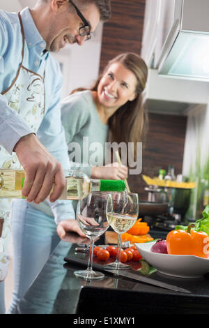 Man pouring white wine in glasses while cooking with woman at kitchen Stock Photo