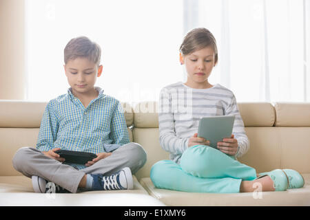 Cute siblings using technologies on sofa at home Stock Photo