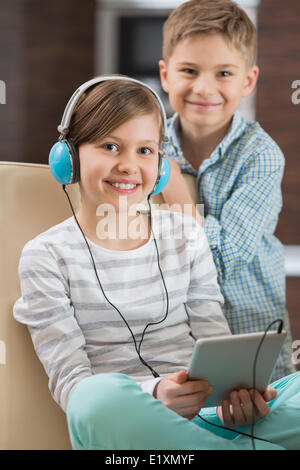 Portrait of cute girl listening music on digital tablet while brother standing behind her Stock Photo