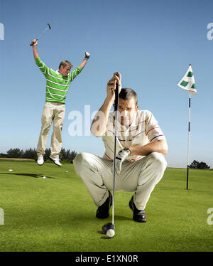 Full length portrait of golfer lining up shot with man jumping in background Stock Photo