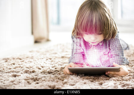 Cute boy using illuminated tablet while lying on rug at home Stock Photo