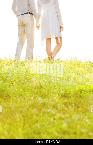 Midsection of couple holding hands while standing on grass against sky Stock Photo