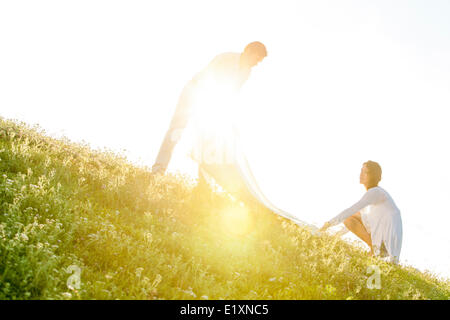 Tilt image of young couple spreading picnic blanket on grass during sunny day Stock Photo