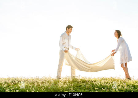 Young couple spreading picnic blanket on grass during sunny day Stock Photo