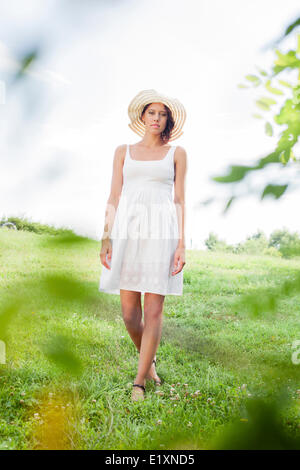 Portrait of young woman in sundress and hat walking in park Stock Photo