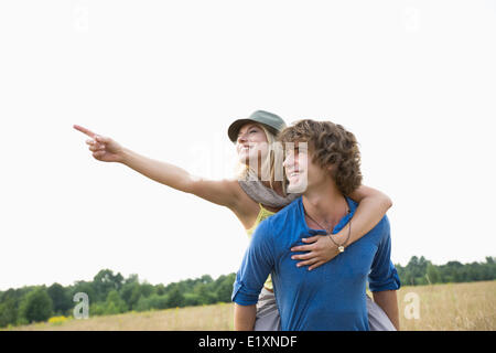 Happy woman showing something while enjoying piggyback ride on man in field Stock Photo