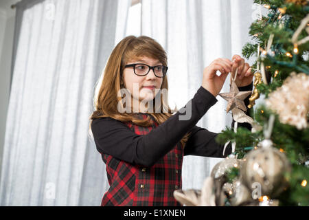 Teenage girl hanging ornament on Christmas tree at home