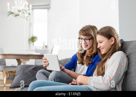 Happy sisters using digital tablet on sofa at home Stock Photo