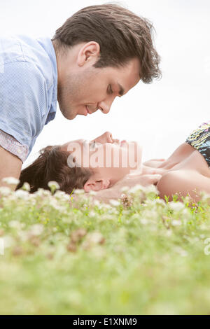 Side view of young man looking at woman sleeping on grass against sky Stock Photo