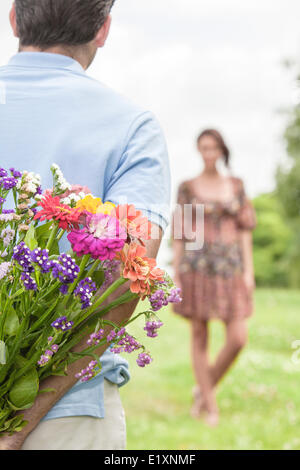 Cropped image of man surprising woman with bouquet in park Stock Photo